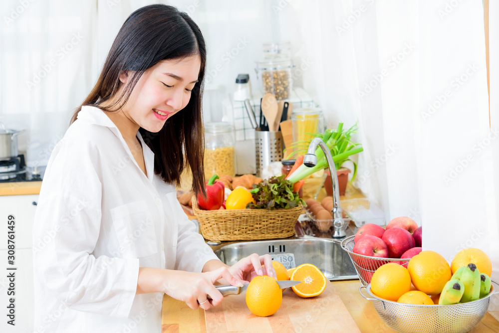 Wall mural happy young girl in kitchen cutting oranges in half for making fresh juice. healthy eating and lifes