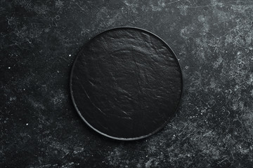 Black plate on black stone background. Top view. Free space for your text.