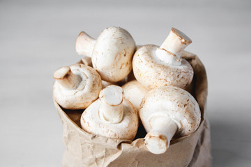 Mushrooms champignons in paper bag on a white wooden table. Close up. Place for text or advertising