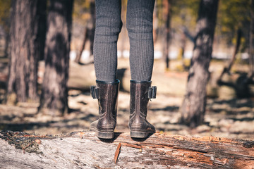 The girls thin legs in rubber boots cross the forest through fallen tree on camping trip.