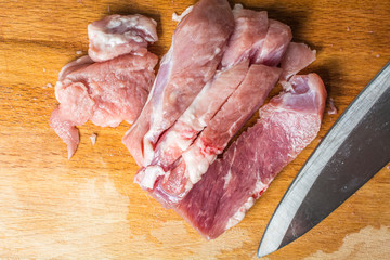 Cut pork meat into pieces with knife on cutting board.