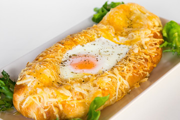 Georgian national pie khachapuri with egg, cheese, butter and salad, on white plate.