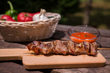 Outdoors summer barbecue, Grilled kebab with vegetables and red sauce on wooden table in the village. Selective focus.
