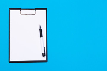 Clipboard with white sheet and pen on a blue background. View from above. space for text