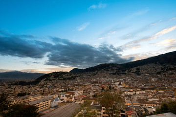 Colonial City of Quito, sunset over the tile roofs, several temples and ancient churches, in the background the monument to the Virgin on the hill called "Panecillo"