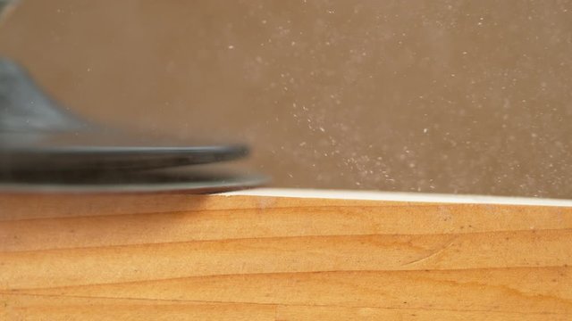 SLOW MOTION, MACRO, DOF: Detailed shot of coarse sandpaper finishing up a carpenter's workpiece. Rotating head of a sanding machine smooths out a wooden board sitting on the carpenter's workbench.
