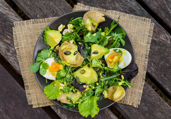 Salad with avocado, dumplings, eggs, pumpkin seeds, arugula and other greens on wooden table in the village. Healthy food concept. Top view.