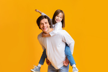 Joyful father and daughter playing together over yellow background