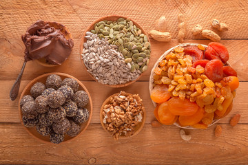 Natural healthy raw energy bites, chocolate paste and mix of dried fruits with nuts on a wooden table. Top view