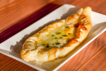 Georgian national pie khachapuri with cheese and butter, on wooden white table in the sunlight.
