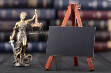 Lady Justice and mini Blackboard on wooden background in front of law books library