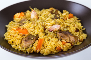Pilaf with lamb, carrots, onions, garlic, pepper and barberry. A traditional dish of Asian cuisine. Selective focus, isolated on brown plate.