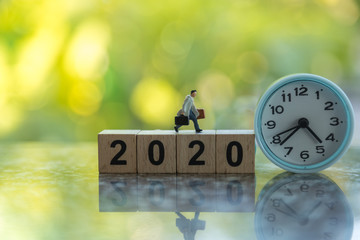 2020 new year and Business Planning concept. Close up of businessman miniature figure with handbag running on wooden number block with round clock and green leaf nature background and copy space.