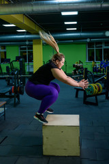 Overweight woman jumps on the box. An obese blonde is trying to lose weight in a circular workout.