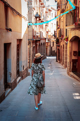 Rear view of a young woman walking in a narrow and old street with garlands of greater celebration...