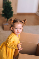 Cute little girl in a yellow dress with two ponytails looks in a box with gifts.