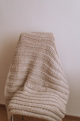 Chair with a knitted plaid on a background of a light wall.