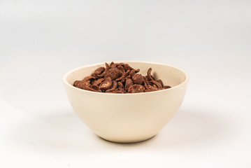Chocolate corn flakes falling to the white bowl isolated on white. Motion.