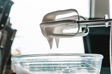Baking concept. Whipped cream of egg whites for perfect peaks in a glass bowl, with a mixer on a...
