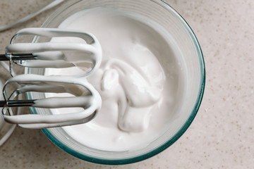 Baking concept. Whipped cream of egg whites for perfect peaks in a glass bowl, with a mixer on a...
