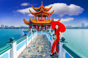 Beautiful Asian Chinese Woman Wearing Cheongsam Traditional Red Dress standing on bridge at Wuliting pavilion,Kaohsiung,Taiwan.