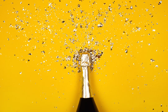 Bottle of champagne with splash of confetti. Flat lay style.