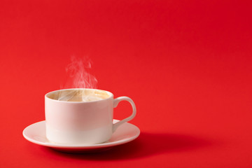 Steaming coffee cup on red background. White сoffee cup with steam. Front view, copy space