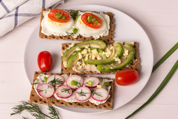 various open sandwiches with cheese, avocado, radish and egg on a white plate, top view