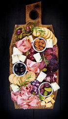 Antipasto platter with ham, prosciutto, salami, cheese,  crackers and olives on a wooden...