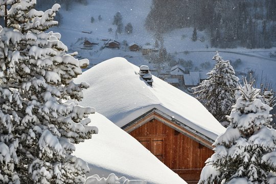 House roof covered with falling snow in a beautiful mountain scenery, idyllic winter atmosphere