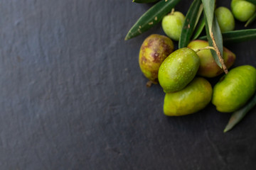 natural olives on black stone background with olive branches and space