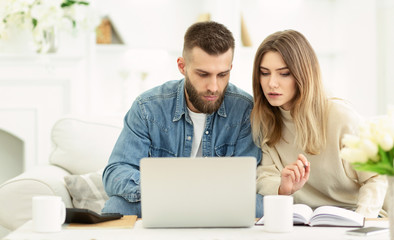 Millennial couple managing expenses with laptop and making notes