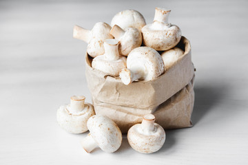 Fototapeta na wymiar Mushrooms champignons in paper bag on a white wooden table. Close up. Place for text or advertising