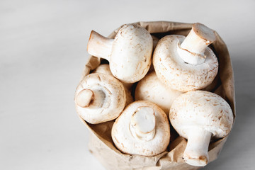 Mushrooms champignons in paper bag on a white wooden table. Close up. Place for text or advertising