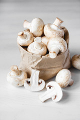 Mushrooms champignons in paper bag on a white wooden table. Close up. Place for text or advertising