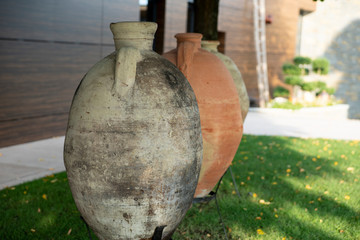 Three huge earthenware jars with a narrow little neck stand on the grass along the side of the building.