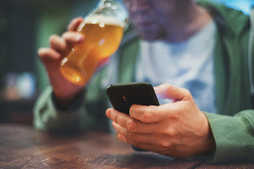 close up of man hand hold smartphone, drinking beer and reading message at bar or pub
