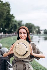 Fototapeta premium Cute brunette girl in a straw hat outdoors. close-up portrait of a young woman . Smiling girl walks around the city in the summer. Active spirit in the park.