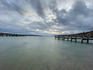 Pier with calm lake "Starnberger See" in Bavaria with smooth cloudy sky