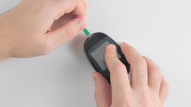 Unrecognized man prepares a glucose meter to measure blood glucose, sugar levels, for measurements. Charges a single strip test into a measuring device. Concept prevention of diabetes.
