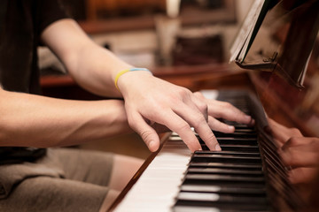 Hands of a young teenage boy playing a familiar melody on the keys of a brown piano