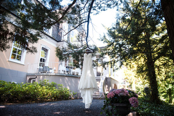 Elegant wedding dress hanging on a tree branch in the garden, near the house