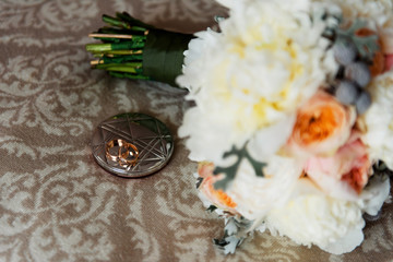Two gold wedding rings on a silver stand. Sideways out of focus a wedding bouquet of different flowers