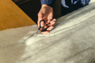 The master cuts scissors from synthetic winterizer for upholstery in the workshop