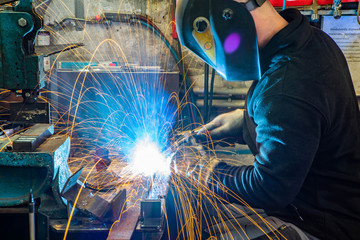 Worker in welding mask at factory. Welding process. Electric welding. Bright yellow sparks.