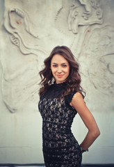 Fototapeta premium Portrait of beautiful brunette sexy woman with fashion makeup on face and long black hair in black dress. girl poses over relief creative background
