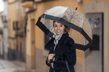 Dark-haired young woman walks through the streets of Caceres with a transparent umbrella on a rainy day