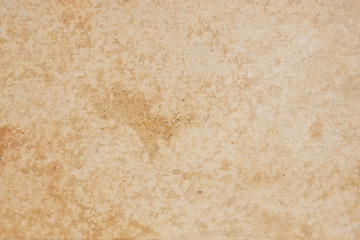 The surface is beige. Cardboard cover of an old book. View from above. Large brown spots, scuffs, stratification of the material. Light background or wallpaper. Reduced contrast. Macro