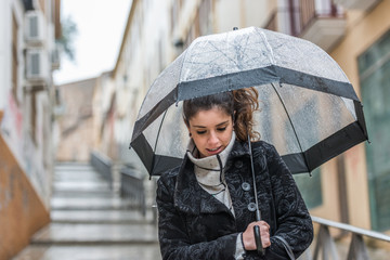 Dark-haired young woman walks through the streets of Caceres with a transparent umbrella on a rainy day