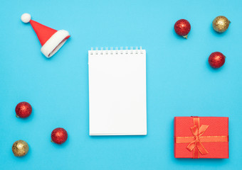 Postcard Happy New Year Flat lay composition with notepad, place for text Christmas decor on blue color background.. santa hat, red gift box. letter